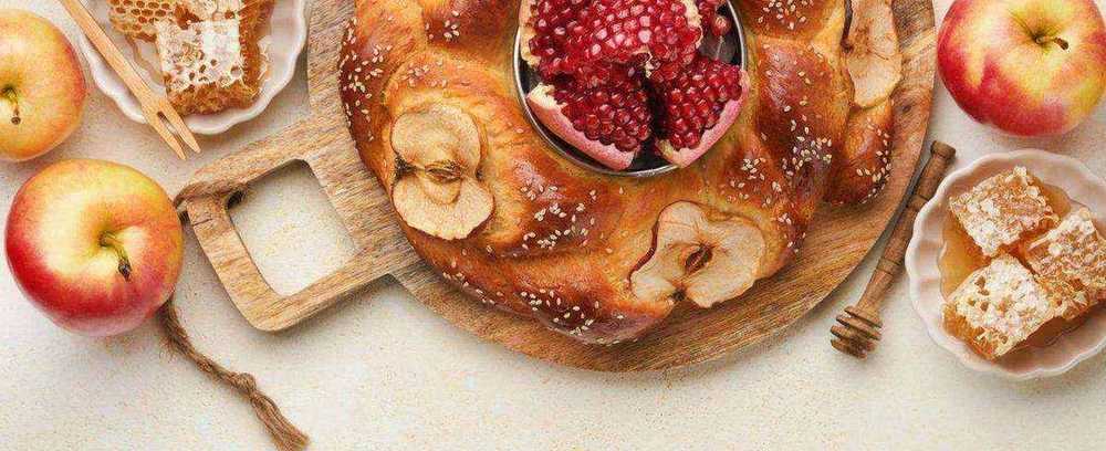 Honeycomb, apples, pomegranate, honey dipper, and baked bread on a rustic table.